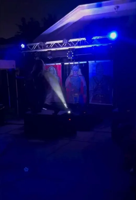 A DJ stage with a lighting truss, blue spotlights and costume character banners set up in front of a house on Fountain Coin Way